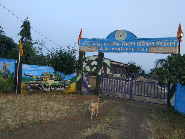The campus gate at Morandhana, Amla, with the school's blue signboard and a painted tank mural on the boundary wall.