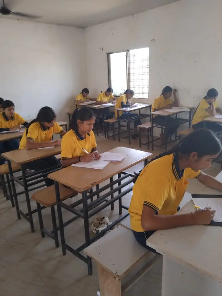 Girls in yellow uniforms write a test at their classroom desks.