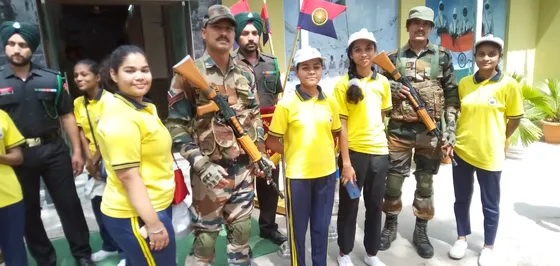 Girl students in yellow T-shirts and white caps stand with Army personnel.