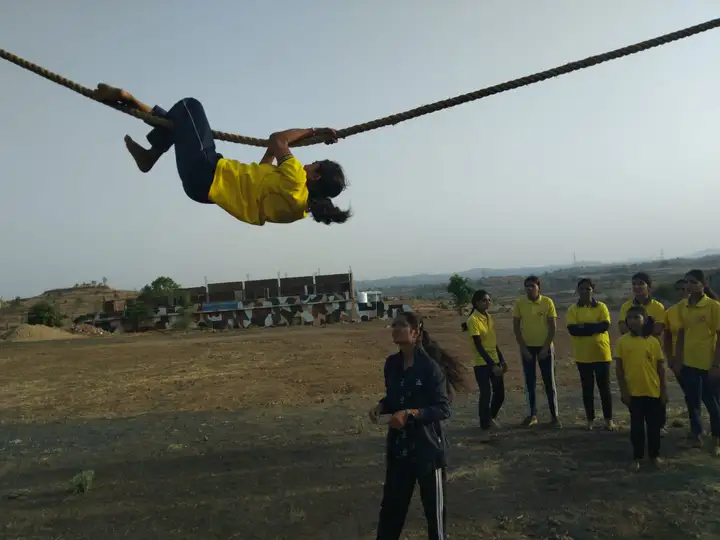 A student in the yellow Ojas T-shirt crosses a rope obstacle while her classmates and instructor watch.